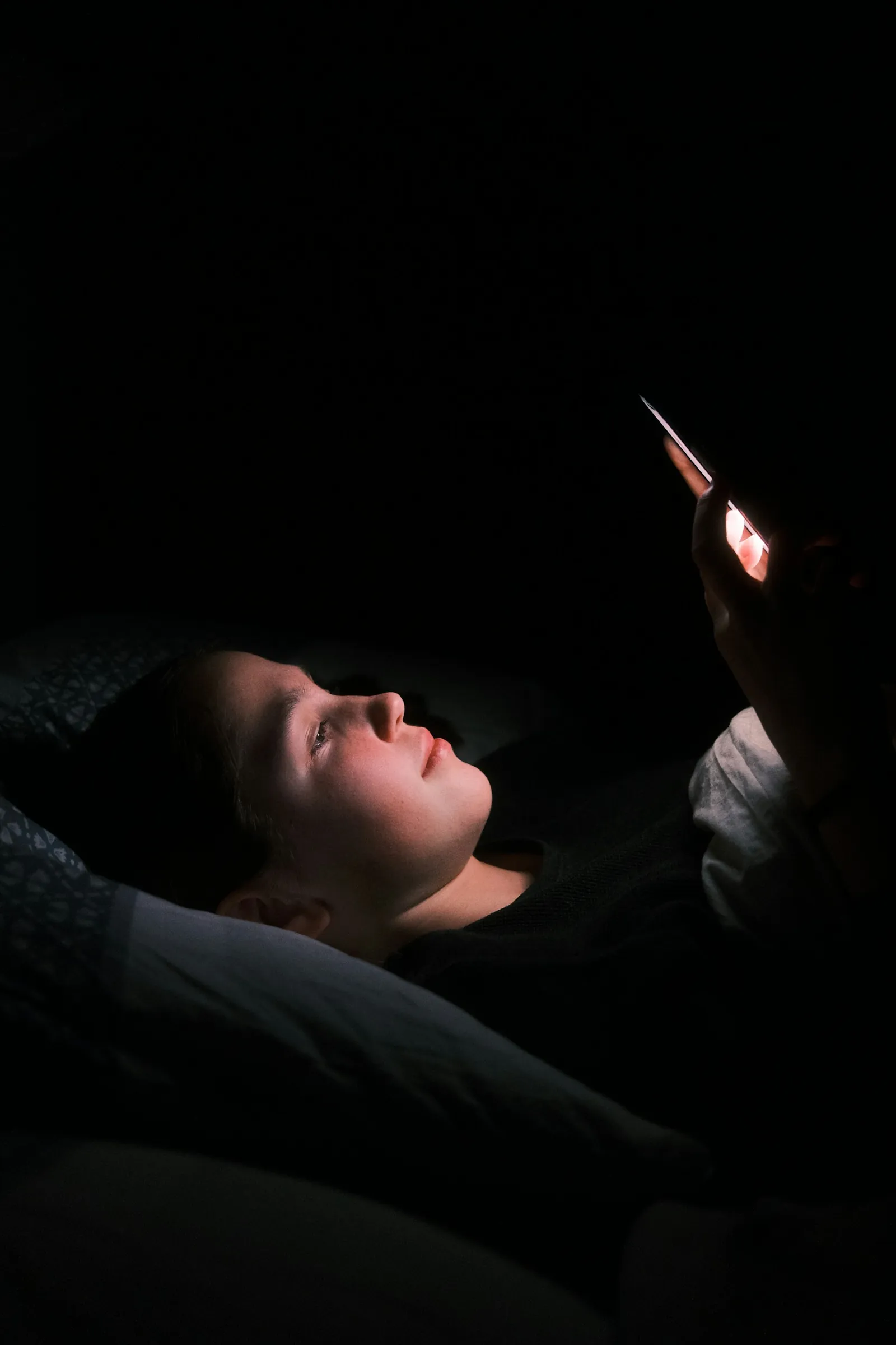 A person in bed at night, face lit by a phone