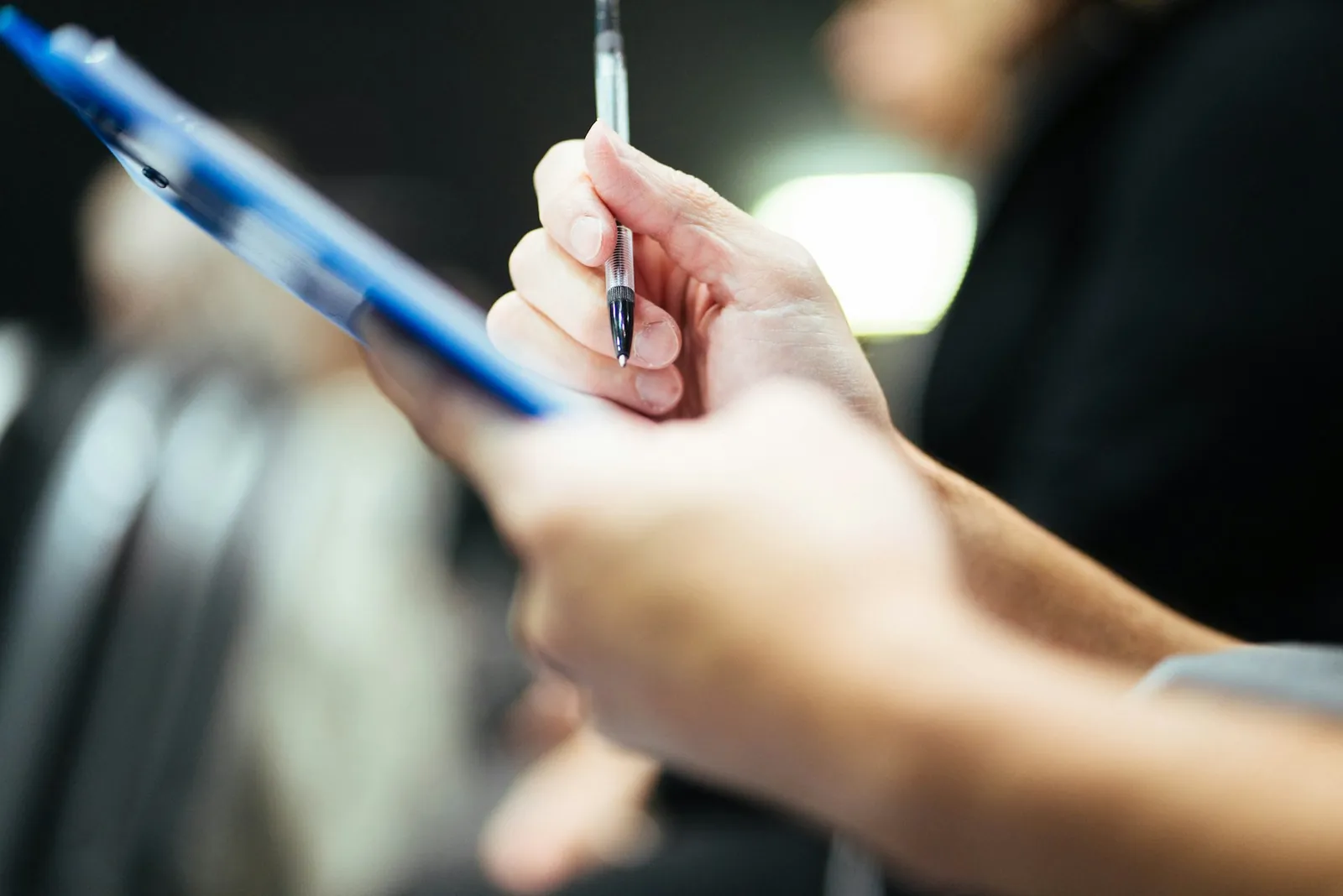 A hand with a pen over a clipboard