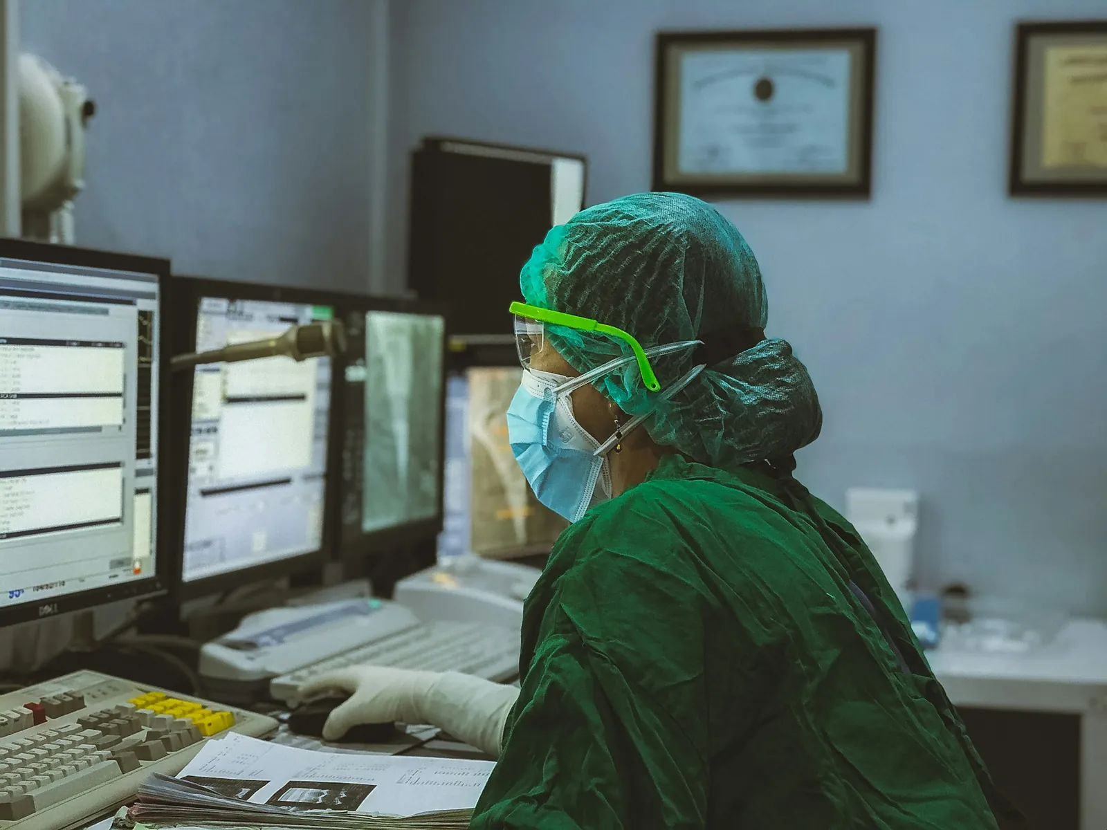 A clinician in surgical scrubs facing a bank of screens