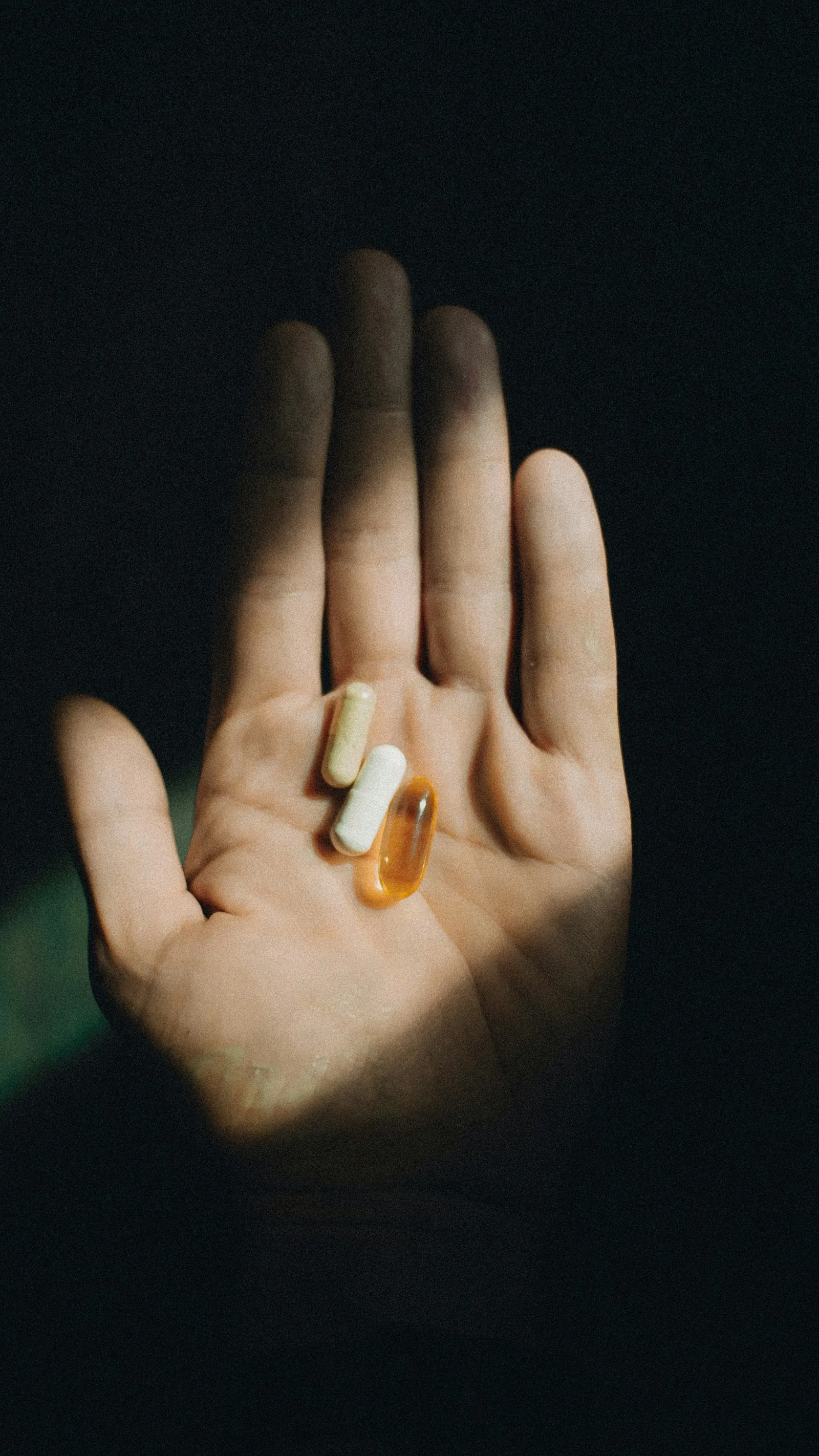An open hand holding three capsules in a shaft of light